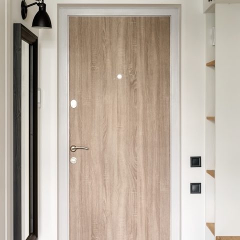 Puerta de madera clara con detalles modernos y espejo lateral.